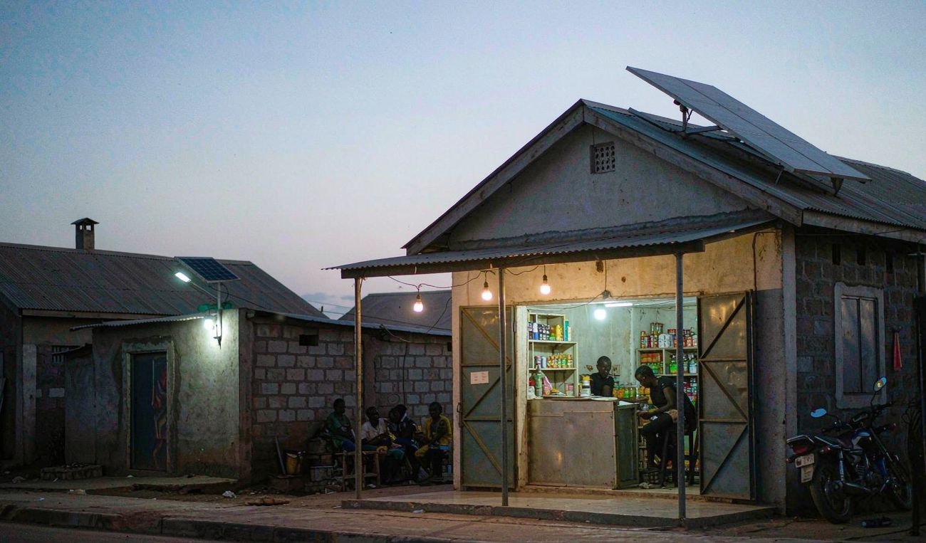 Small roadside shop and home at dusk, warmly lit by solar-powered LED lights — AI-generated illustrative scene